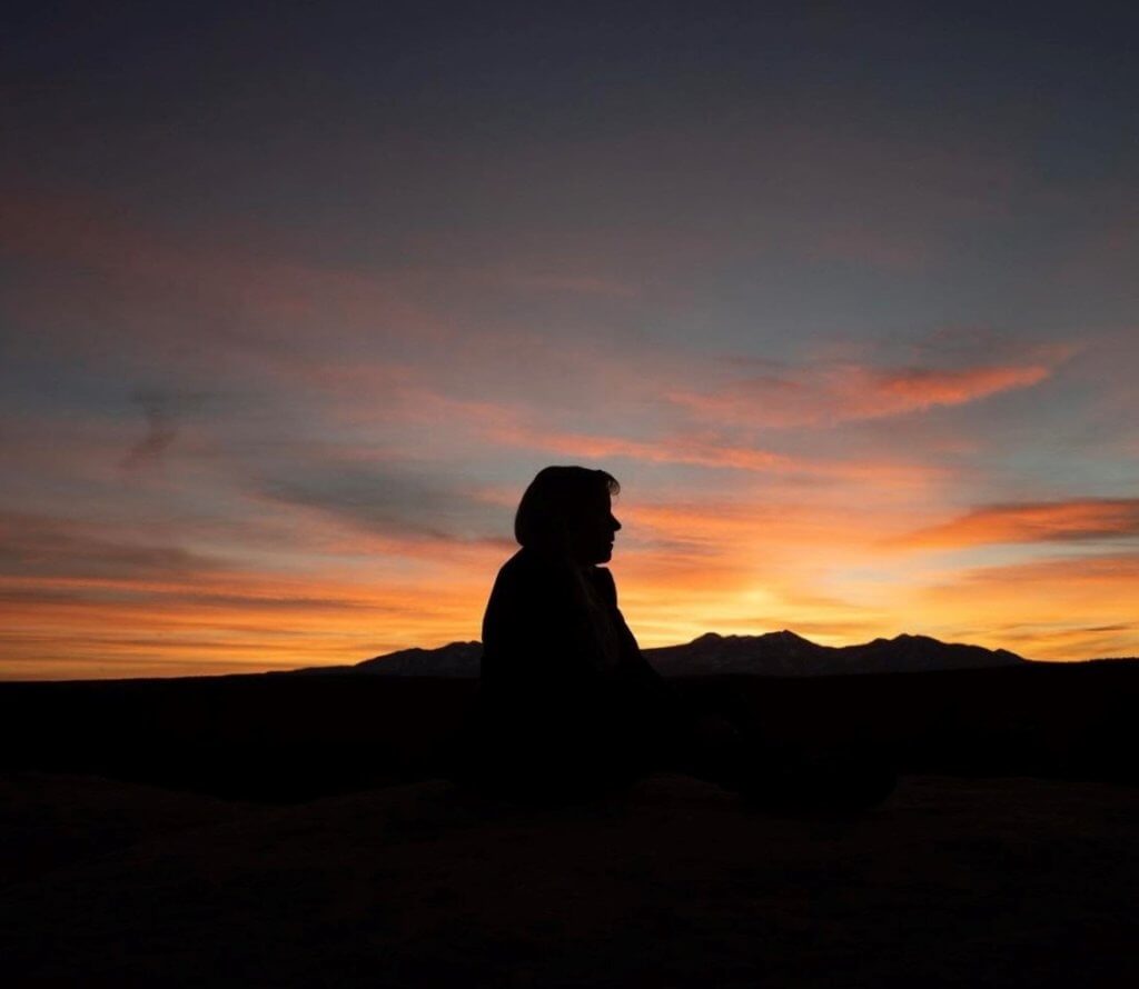 A silhouette of Barb sits in a canyon at Sunset.