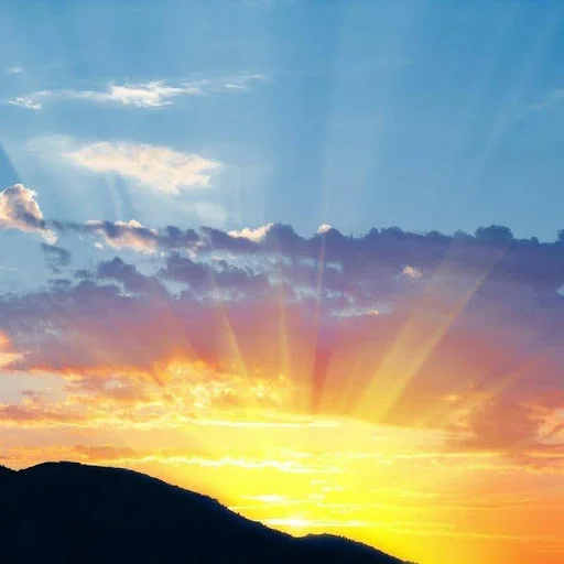 sun setting behind mountain with light shining upward through clouds