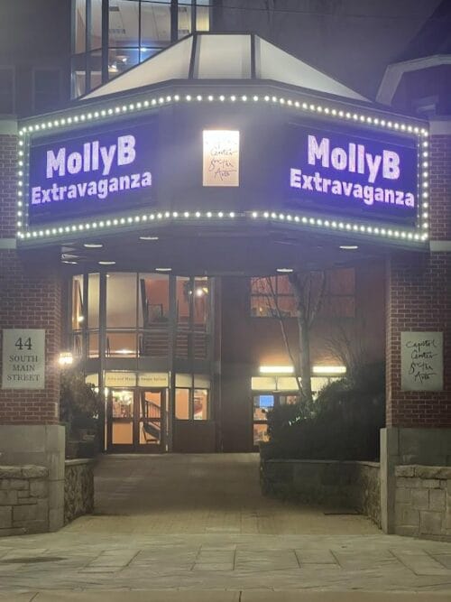 The marquee glows with "MollyB Extravaganza" at the venue entrance, as brilliant lights illuminate the sign, setting the stage for an unforgettable MollyBanzoff fundraiser night.